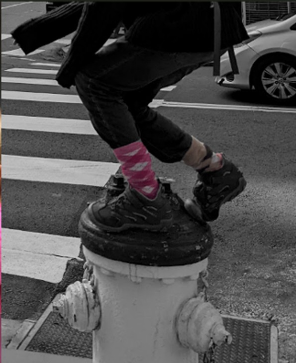 A kid's feet standing atop a fire hydrant. All but the socks going into the boots are black and white. The colorful socks don't match.